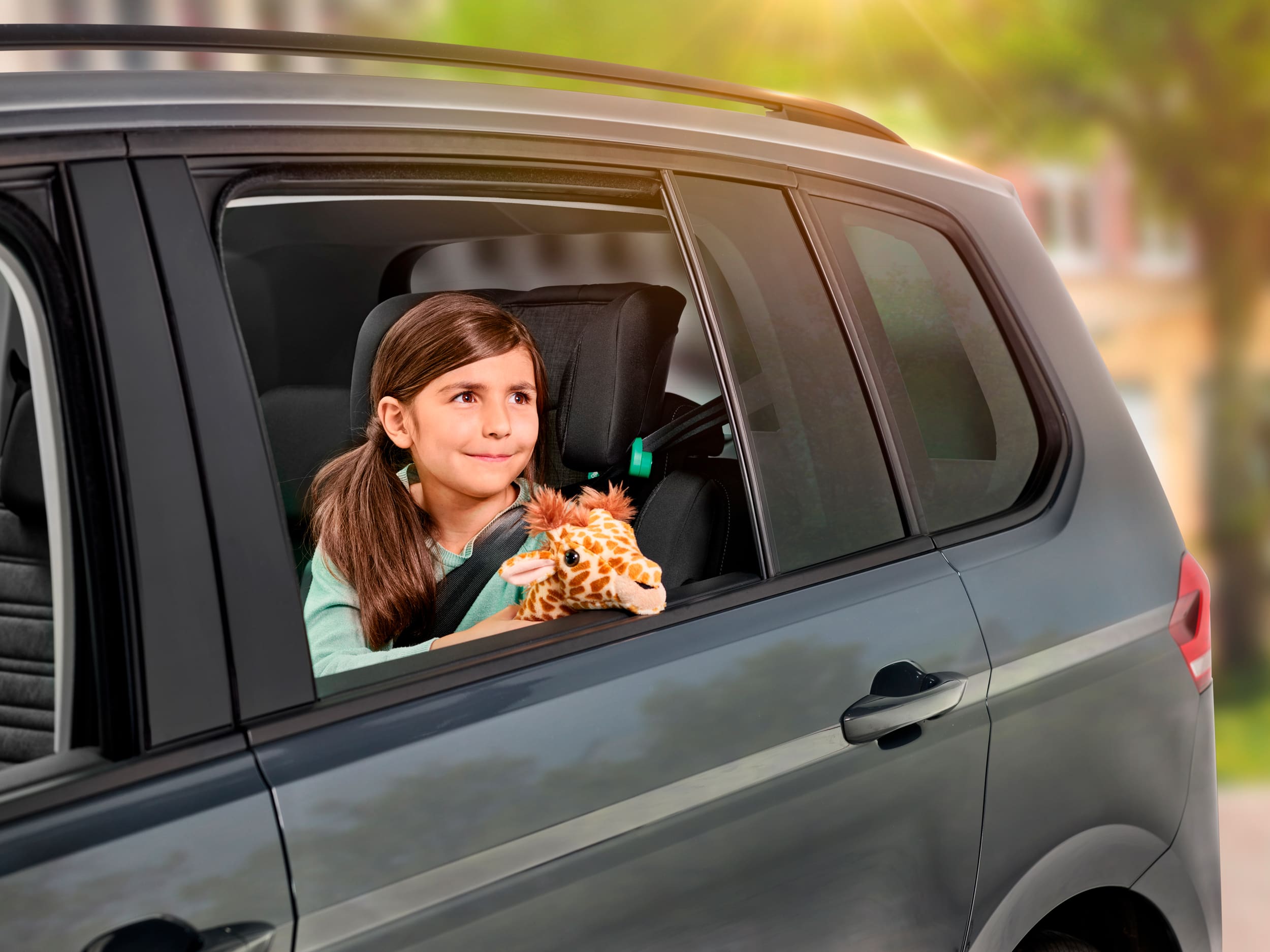 Kind blickt aus Autofenster mit Stofftier.